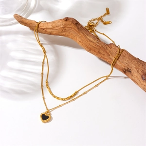 Double-layered gold stainless steel necklace with black heart pendant on a wooden branch