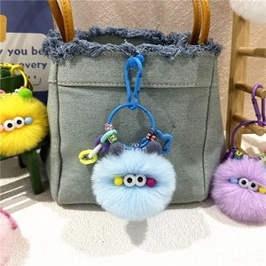 Close-up of colorful plush monster charms with large eyes and letter beads on a denim bag