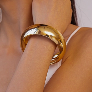 Detail of chunky gold wide cuff bracelet with polished mirror finish on model's wrist