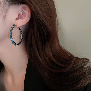 Detail of large twisted hoop earring with blue rhinestones worn by a fashion model