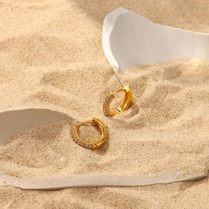 Close-up of 18K gold-plated earrings with clear zircons on sand for a summer aesthetic