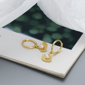 Macro detail of gold shell earrings with white pearl accent on textured background