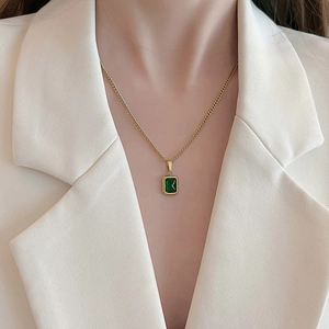 Gold titanium necklace with emerald green rectangular pendant worn on white suit