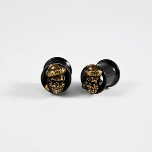 Detail of black hollow ear gauges with golden skull inlay for ear stretching