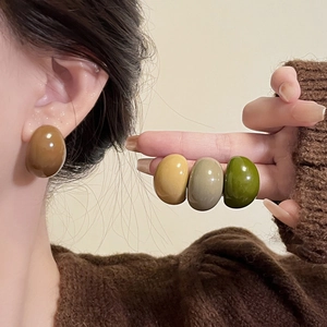 Close-up of glossy geometric resin C-shaped stud earrings in earthy brown and green tones