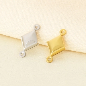 Detailed view of diamond-shaped gold and silver metal pendants on beige fabric