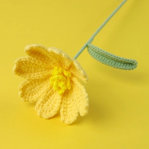 Macro detail of hand-crocheted yellow daisy flower with knitted texture and green stem