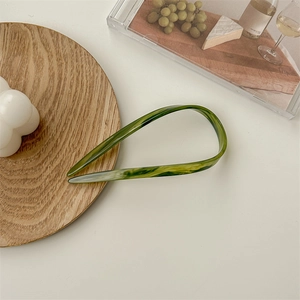 Detail of green tortoiseshell acetate U-shaped hair pin on a minimalist setup