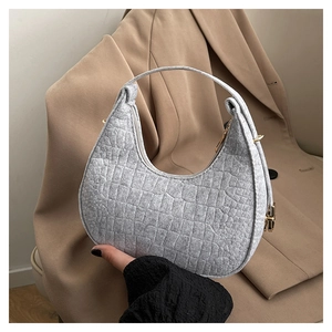 Close-up of grey quilted felt handbag with gold hardware held against a beige blazer