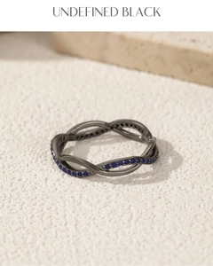 Detail of twisted black metal ring featuring pavé set blue gemstones on a textured surface