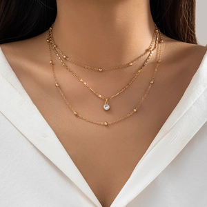 Detailed view of triple-layered gold chain necklace with beads and a round pendant