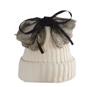 White knitted beanie with oversized black lace bow and gold embroidery on white background