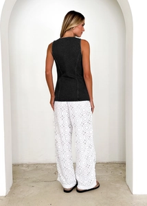 Detail of dark grey sleeveless denim vest and white floral lace wide-leg pants on model