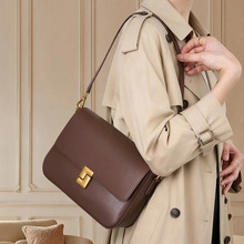 Detail of dark brown leather crossbody bag with square gold buckle on beige trench coat