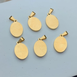 Set of six oval golden stainless steel Guadalupe pendants on a white textured surface