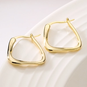Minimalist gold-plated geometric earrings displayed on a white textured ceramic plate