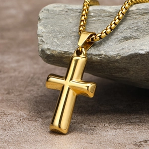 Close-up of a polished gold stainless steel cross pendant on a textured grey rock surface