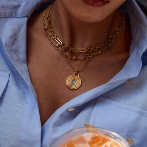 Detail einer dreilagigen Goldkette mit blauem Steinfederanhänger, getragen am Modell