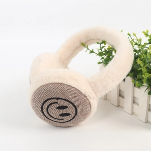 Dettaglio di paraorecchie in peluche beige con motivo sorridente su tessuto a spina