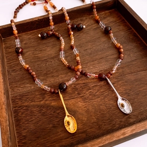 Détail des pendentifs cuillère vintage sur colliers en perles de bois or et argent
