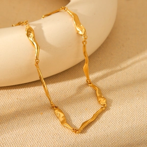 Close-up of golden irregular hammered link necklace on a white ceramic display
