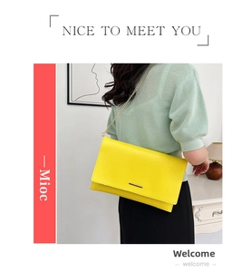 Close-up of bright yellow minimalist clutch bag featuring a sleek gold metal bar and chain strap