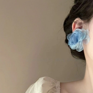Gros plan de grandes boucles d'oreilles fleurs en tulle bleu portées par un modèle