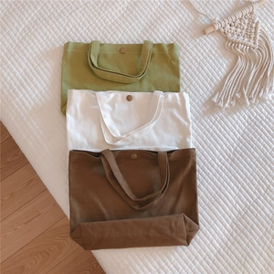 Overhead view of minimalist canvas tote bags in olive, white and brown with snap buttons