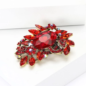 Detailed close-up of a red crystal brooch with vintage bronze alloy setting and floral patterns