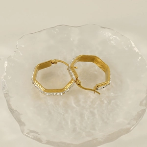 Detailed view of gold geometric earrings with sparkling diamonds on ice glass