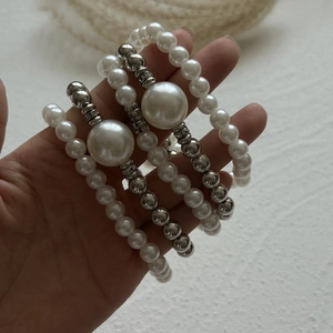 Detail of layered silver beaded bracelets with large faux pearls held in hand