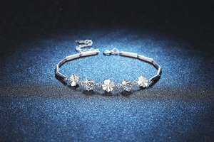 Macro shot of silver four-leaf clover bracelet with D color moissanite on blue background