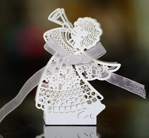 Macro detail of laser-cut white angel favor box with intricate floral patterns and ribbon