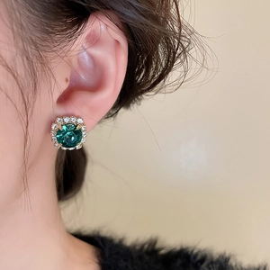 Gros plan d'une boucle d'oreille en pierre verte avec halo de diamants sur l'oreille