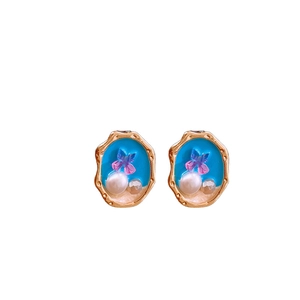 Orecchini vintage dorati con smalto blu, motivo a farfalla e perle su uno sfondo bianco