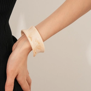Detail view of a resin bangle with marble texture worn by a model in chic beige