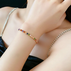 Close-up of a gold-plated rainbow gemstone bracelet worn on a wrist with black background