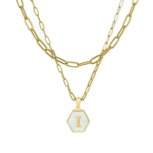 Macro detail of gold paperclip chain and hexagonal shell pendant with letter I
