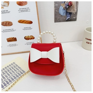 Detail of red kids crossbody bag with large white bow and elegant pearl handle