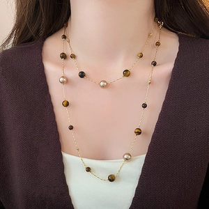 Detail of layered gold necklace with brown tiger eye beads on a model wearing knitwear