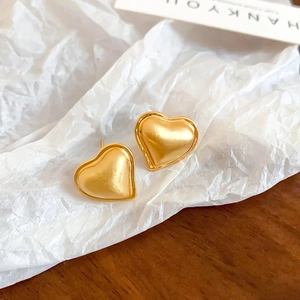 Macro shot of minimalist gold heart stud earrings with a brushed metal matte texture