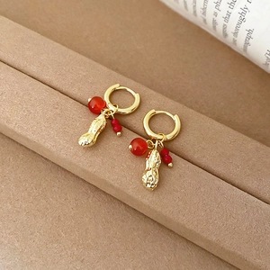 Detailed close-up of golden peanut drop earrings with red crystal beads and hoop design