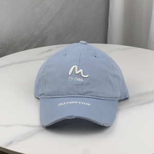 Light blue embroidered baseball cap with M logo and distressed brim on marble surface