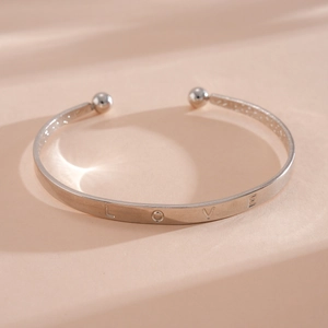 Detailweergave van een zilveren armband met LOVE-gravure en decoratieve kogeluiteinden.