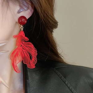 Close-up of a model wearing red hollow goldfish drop earrings with golden accents