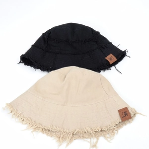 Detail of frayed edges and brown leather logo patch on canvas bucket hats in beige and black
