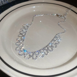 Close-up of sparkling silver rhinestone necklace in hollow lace design on a white plate
