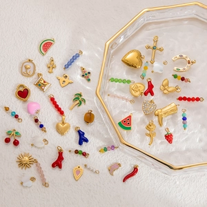 Close-up of assorted gold DIY charms with butterfly and fruit designs on a glass tray
