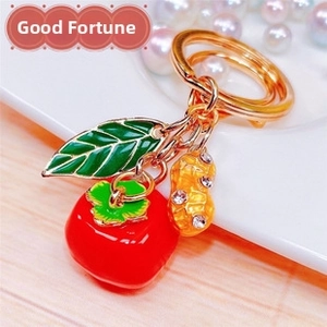 Detail of a red persimmon and crystal peanut keychain with gold plating and enamel