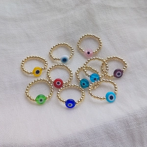 Colorful evil eye beaded rings with 18K gold-plated beads on white fabric